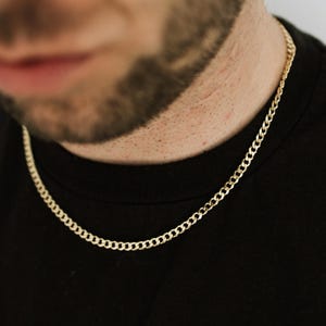 May include: A gold chain necklace worn by a person with a black shirt.