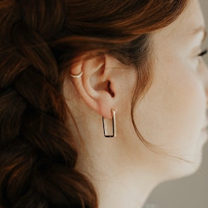 May include: A pair of gold rectangle hoop earrings. The earrings are simple and elegant, and would make a great addition to any jewellery collection.