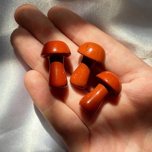May include: Three red jasper mushroom shaped stones. The stones are polished and have a smooth, glossy finish.