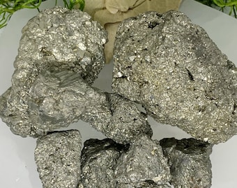 May include: A collection of raw pyrite crystals, also known as fool's gold, in various sizes and shapes. The crystals have a metallic, gold-like appearance with a rough, textured surface.