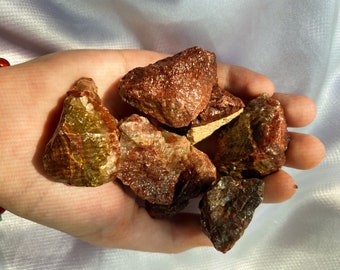 May include: A collection of rough, red and green gemstone crystals. The crystals are various sizes and shapes.