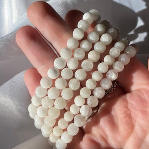 May include: A stack of white moonstone bead bracelets. The bracelets are made of round, smooth beads and are stacked on top of each other.