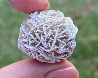 May include: A white rose quartz crystal, also known as a desert rose, with a delicate, layered structure. The crystal is about the size of a golf ball and has a natural, rough texture.
