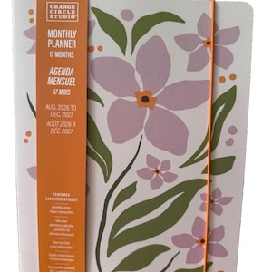 May include: A 17-month monthly planner by Orange Circle Studio with a white cover featuring a floral pattern of light purple flowers and green leaves. An orange vertical band wraps around the left side with text, and an orange elastic band closure.