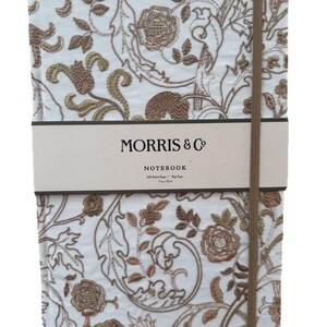 May include: A notebook with a cream-colored cover featuring an embroidered floral design in shades of brown and gold. The notebook has a brown elastic closure and a band with the text "MORRIS & Co NOTEBOOK". The notebook measures 7 x 10 inches.