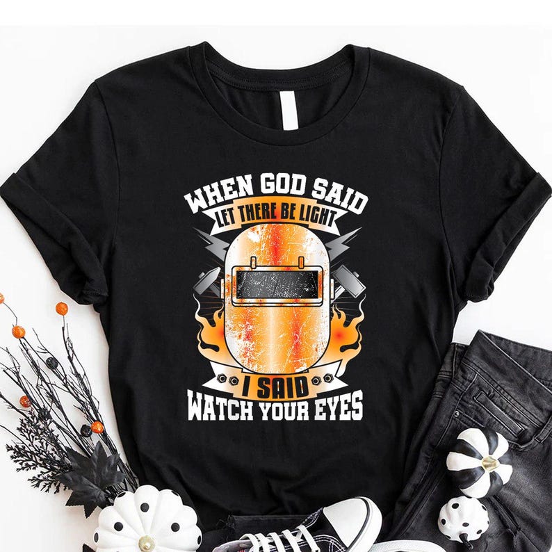 May include: Black t-shirt with a welding mask graphic and the text "When God said let there be light I said watch your eyes".