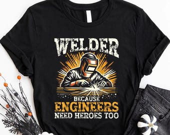 May include: Black t-shirt with a graphic of a welder with the text "Welder Because Engineers Need Heroes Too".