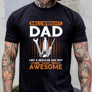 Peut inclure: T-shirt noir avec du texte blanc qui dit "Millwright Dad Like a Regular Dad But More Awesome". Le texte est entouré d'un motif de points orange. Il y a trois outils au centre du texte.