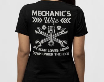 Puede incluir: Camiseta negra con un gráfico blanco que dice "Mechanic's Wife" con llaves y un motor. El texto debajo dice "My man loves going down under the hood."