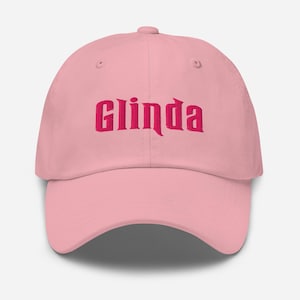 May include: A light pink baseball cap featuring the word Glinda embroidered in dark pink thread across the front center. The cap has a structured crown, a curved brim, and a button at the top, showcasing a classic six-panel design.