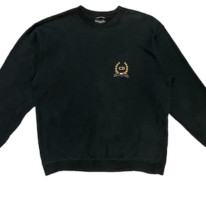 Può includere: Felpa nera girocollo a maniche lunghe. Presenta un piccolo stemma ricamato sul petto con dettagli oro, rossi e bianchi. Il marchio è visibile sul colletto. Un capo d'abbigliamento vintage.