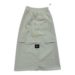 May include: A cream-colored midi skirt featuring an elasticized waistband with a drawstring, a large flap pocket on the front, and a rectangular black Fila brand patch centered on the lower portion of the garment. The skirt has a straight silhouette.