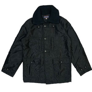 May include: Black jacket with a ribbed knit collar and button-down front. The jacket has four front pockets and buttoned cuffs. The label on the collar reads "UNITED CARR".