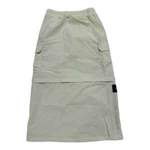 May include: A cream-colored midi skirt featuring an elastic waistband, two side cargo pockets with flaps, and a small rectangular black brand label on the lower right side. The skirt has a layered design with a straight silhouette and smooth fabric.