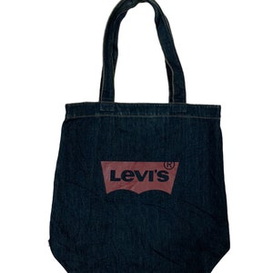 May include: A dark blue denim tote bag with two matching handles. The bag features a large, red Levi's logo on the front. The bag is made of a sturdy denim material and is designed for carrying items.