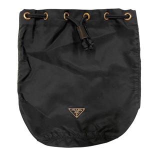 May include: Black drawstring bag with gold-tone eyelets and a black drawstring closure. The bag features a small gold Prada logo on the front. The bag is made of a smooth, possibly nylon, material.
