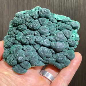 May include: A vibrant green malachite specimen with a bubbly, textured surface. The natural stone displays a range of green hues, from deep forest to lighter shades. The mineral's unique formation is visible, showcasing its organic, layered structure.