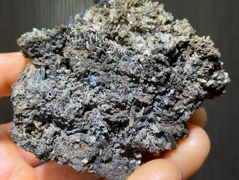 May include: A close-up of a mineral specimen featuring a matrix of dark gray and black crystals. The surface is textured with clusters of smaller, clear and white crystals. The overall appearance is rough and natural.