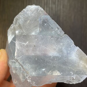 K&ouml;nnte beinhalten: Ein gro&szlig;er, durchscheinender, hellblauer Kristall mit einer rauen, facettierten Oberfl&auml;che. Der Kristall hat eine geometrische Form mit sichtbaren inneren Strukturen und einem leichten Gelbstich an einer Kante. Das Gesamtbild ist kristallin und nat&uuml;rlich.