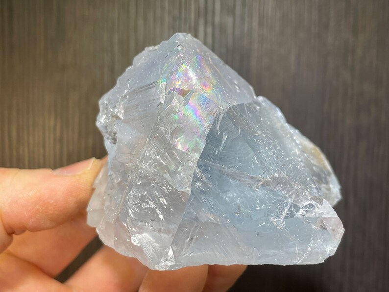 K&ouml;nnte beinhalten: Eine durchscheinende, hellblaue Kristallformation mit rauer, strukturierter Oberfl&auml;che. Der Kristall zeigt schillernde Regenbogenfarben, wo sich das Licht durch seine Facetten bricht. Die Gesamtform ist eckig und unregelm&auml;&szlig;ig.