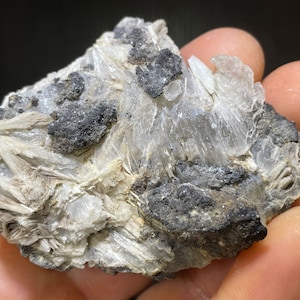 May include: A close-up of a mineral specimen featuring a combination of crystalline and amorphous structures. The specimen displays translucent, layered formations in shades of white and gray, interspersed with dark, irregular patches.