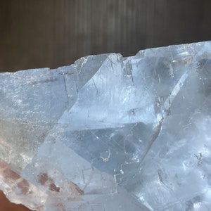 K&ouml;nnte beinhalten: Nahaufnahme einer durchscheinenden, hellblauen Kristallformation. Der Kristall hat eine geschichtete, geometrische Struktur mit scharfen Kanten und einer leicht rauen Textur. Das Licht f&auml;ngt die Facetten ein und erzeugt Glanzlichter.