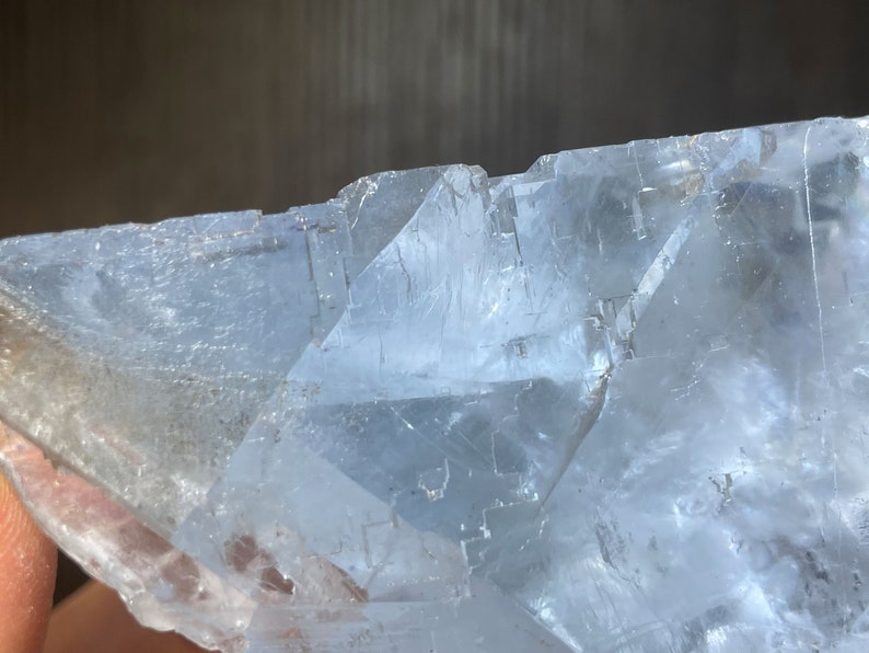 K&ouml;nnte beinhalten: Nahaufnahme einer durchscheinenden, hellblauen Kristallformation. Der Kristall hat eine geschichtete, geometrische Struktur mit scharfen Kanten und einer leicht rauen Textur. Das Licht f&auml;ngt die Facetten ein und erzeugt Glanzlichter.