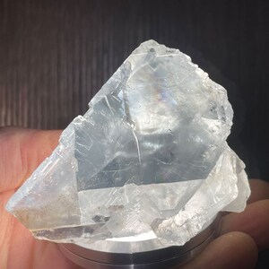K&ouml;nnte beinhalten: Ein durchscheinendes, kristallines Mineralexemplar. Das hellfarbene, unregelm&auml;&szlig;ig geformte Gestein hat eine raue, strukturierte Oberfl&auml;che mit sichtbaren inneren Strukturen. Das Mineral wird auf einer silberfarbenen Basis gehalten.