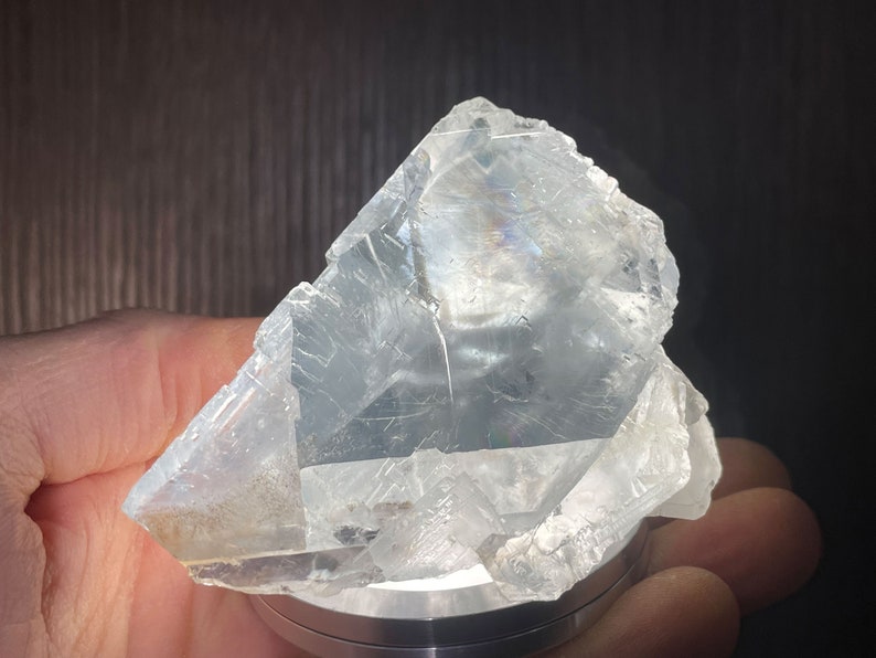 K&ouml;nnte beinhalten: Ein durchscheinendes, kristallines Mineralexemplar. Das hellfarbene, unregelm&auml;&szlig;ig geformte Gestein hat eine raue, strukturierte Oberfl&auml;che mit sichtbaren inneren Strukturen. Das Mineral wird auf einer silberfarbenen Basis gehalten.