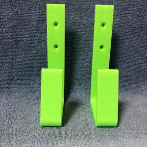 May include: Two lime green wall mounted hooks with two holes each. The hooks are made of a textured material.