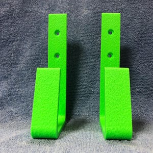May include: Two bright green metal wall hooks with two holes for mounting. The hooks are shaped like a U and have a textured surface.
