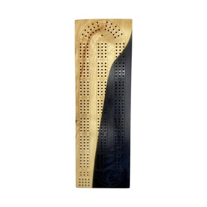 May include: A wooden cribbage board with a black epoxy resin inlay. The board has a traditional cribbage design with numbered holes and a scoring track.