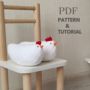 May include: Two white plush chicken-shaped slippers with red combs and orange beaks sit on a white chair. The chair has light wood legs and a white seat. The text "PDF PATTERN & TUTORIAL" is in the background.