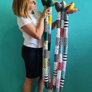 May include: Two long, colorful fabric snakes with patchwork patterns. The snakes have green and yellow heads with red tongues. The bodies are made of various fabric squares in patterns like stars, polka dots, and stripes. The snakes are held up by a person.