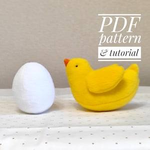 Op de afbeelding: Een geel vilt kuiken speelgoed met zwarte ogen en een oranje snavel, naast een wit vilt ei. De tekst "PDF pattern & tutorial" is in zwart boven het kuiken geschreven.