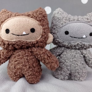 May include: Two plush toys, one brown and one gray, with furry textures and smiling faces. They have large, round eyes and a single white tooth showing in their smiles.