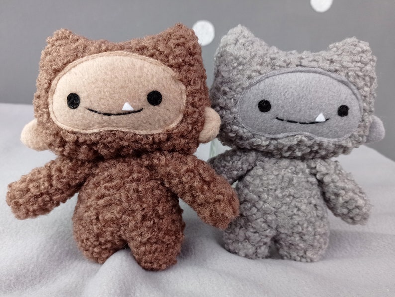 May include: Two plush toys, one brown and one gray, with furry textures and smiling faces. They have large, round eyes and a single white tooth showing in their smiles.