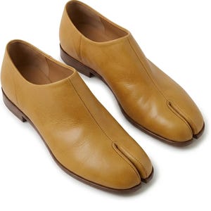 Op de afbeelding: Een paar mosterdgele leren schoenen met een opvallend ontwerp met gespleten teen. Deze instapschoenen hebben een gladde leren bovenkant, een laag profiel en een donkerbruine zool met een kleine hak, met een strakke en eenvoudige vormgeving.
