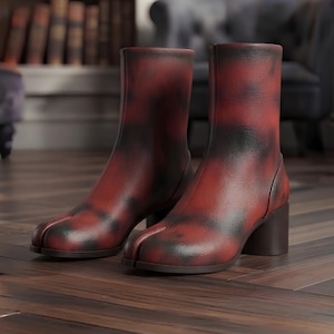May include: A pair of ankle boots featuring a distinct split-toe design, crafted from leather with a mottled red and black finish. These boots have a mid-height block heel and a smooth, structured shaft that rises above the ankle.