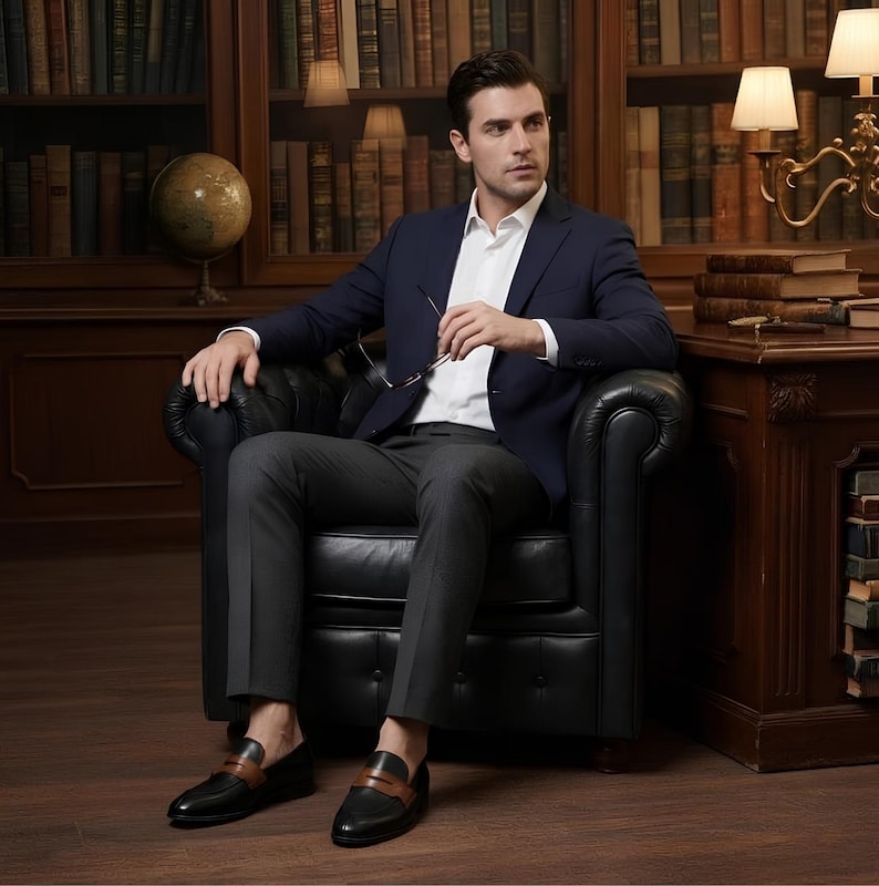 May include: A navy blue blazer, white button-down shirt, and dark gray trousers paired with black and brown leather loafers. The attire features a structured jacket, a crisp collared shirt, tailored pants, and two-tone slip-on shoes with a strap.