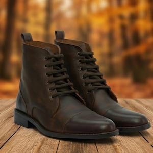 Peut inclure: Une paire de bottes en cuir marron avec un laçage. Les bottes ont un style classique avec un bout arrondi et une semelle robuste. Les bottes sont présentées sur une surface en bois avec un arrière-plan flou de feuillage d'automne.