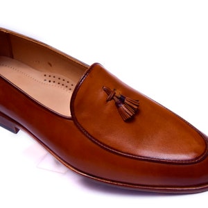 May include: A pair of brown leather tassel loafers. The loafers have a pointed toe and a slip-on design.