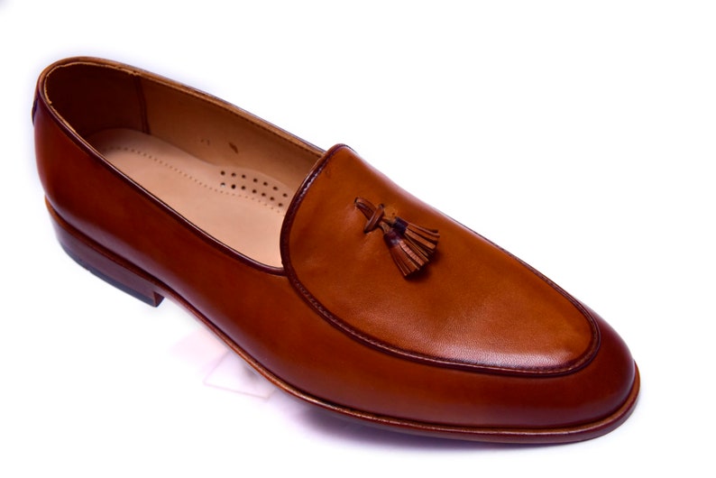 May include: A pair of brown leather tassel loafers. The loafers have a pointed toe and a slip-on design.