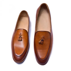 May include: A pair of brown leather loafers with tassel accents. The loafers have a pointed toe and a low heel.