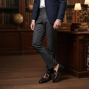 May include: A pair of charcoal gray trousers worn with a navy blue blazer, a white shirt, and black leather loafers featuring a brown leather strap across the top. The trousers have a straight-leg cut and a clean, tailored appearance.