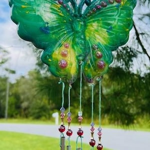 May include: A green butterfly wind chime with iridescent accents and red beads hanging from silver tubes.