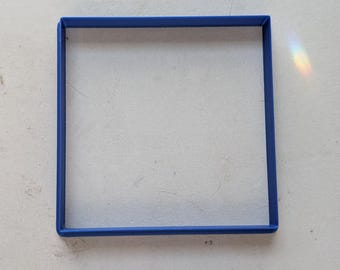 May include: A square, blue frame sits on a white, textured surface. The frame is a solid, vibrant blue, and the surface has subtle imperfections. Light refracts, creating a rainbow effect.