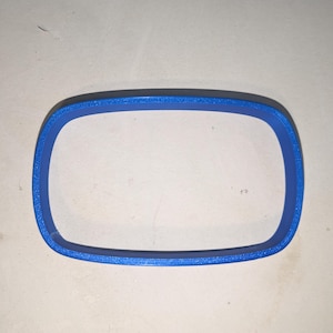 Può includere: Un oggetto rettangolare blu con angoli arrotondati. L'oggetto è di colore pieno e sembra essere fatto di plastica o materiale simile. La forma è un design geometrico semplice.