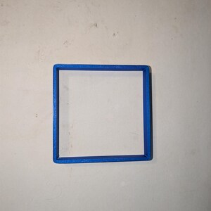 May include: A square, blue, 3D-printed object. The object is a hollow square frame, with a solid blue border. The frame is centered on a light gray surface.