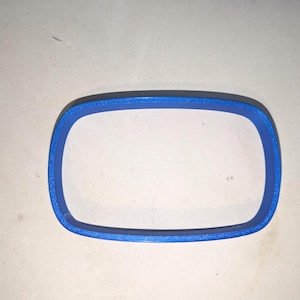 May include: A blue rectangular cookie cutter with rounded corners. The object features a solid, continuous frame with a smooth, flat top edge and a slightly textured side surface, forming a simple, open-centered shape for cutting dough.